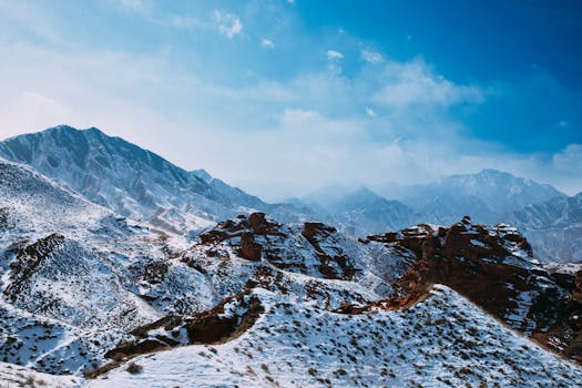 Scenic view of shiny rough snowy mountains with faded grass under colorful sky in mist in wintertime