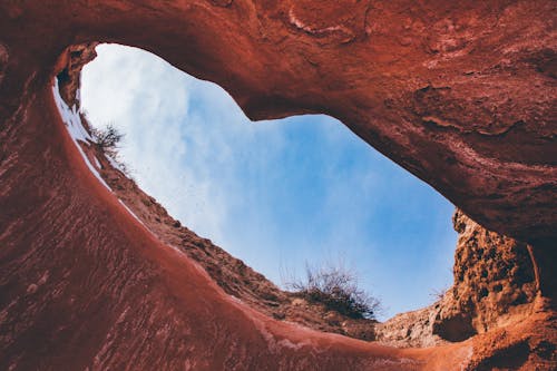 From below of natural rough hole in rocky formation under blue cloudy sky in daytime