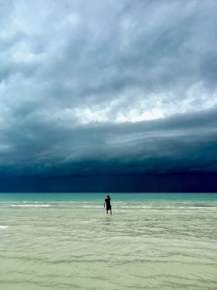 Person Walking On Beach Under Cloudy Sky