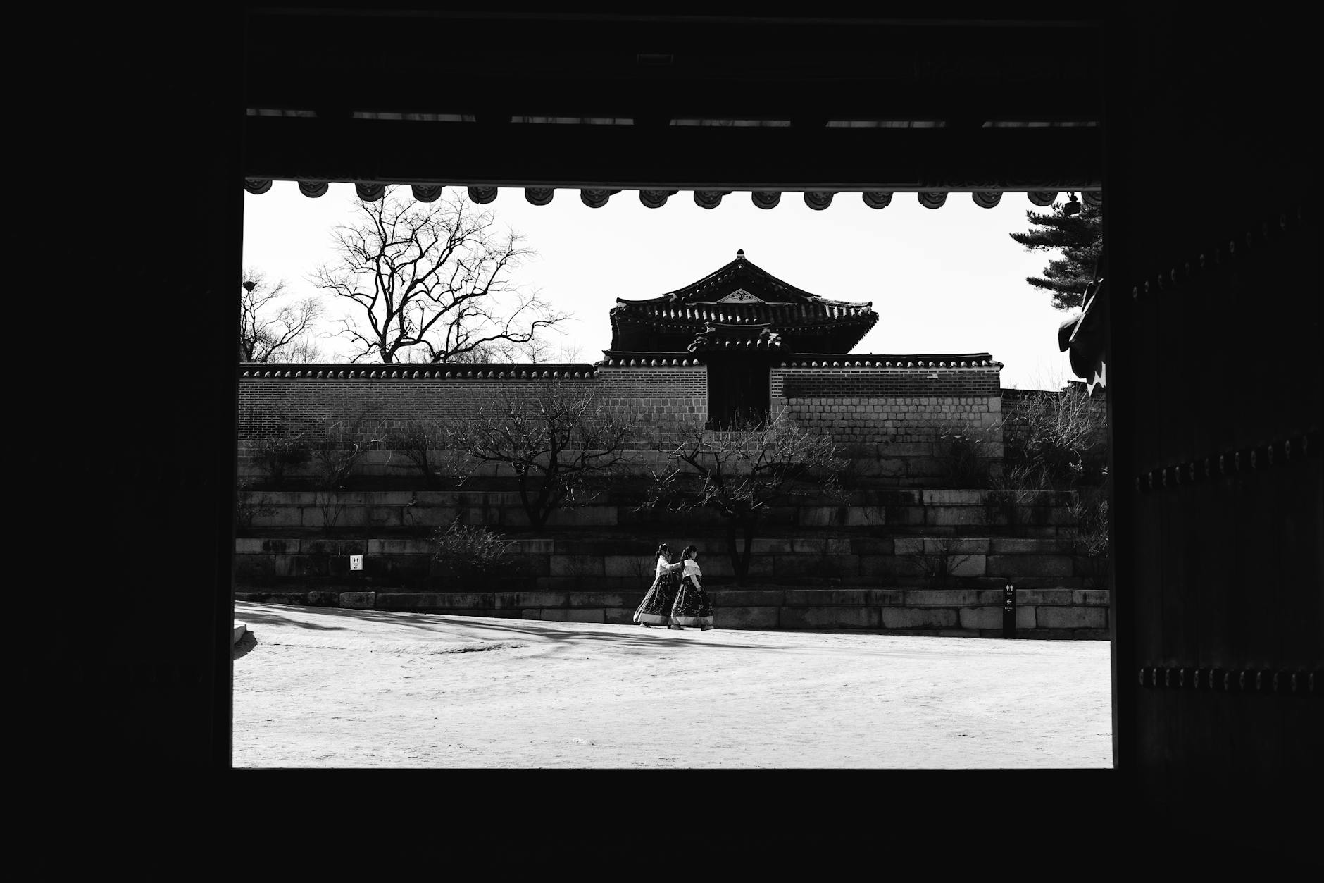 A black and white view of a traditional palace in Seoul, framed by a wooden gate, capturing a serene winter scene.