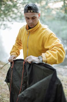 白天，一名穿着黄色夹克的年轻人在森林里搭起了帐篷