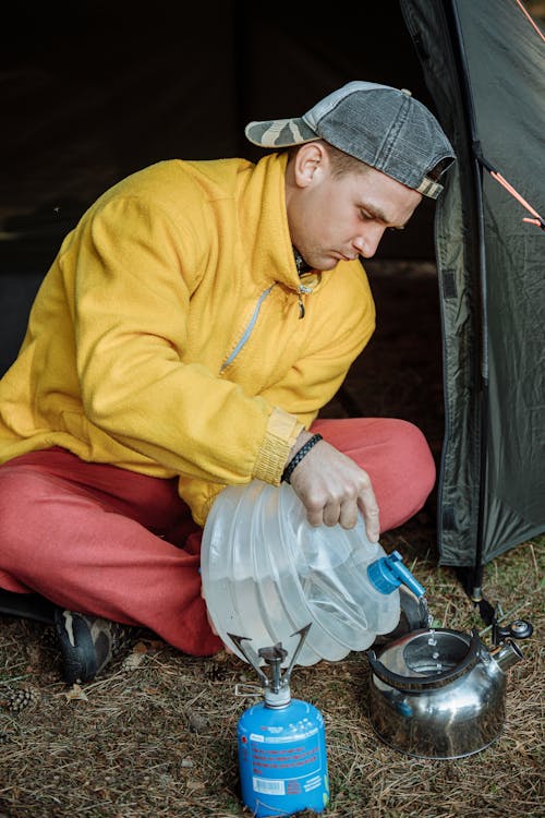 Uomo In Felpa Con Cappuccio Gialla E Pantaloni Rossi Seduto A Terra Accanto Alla Tenda