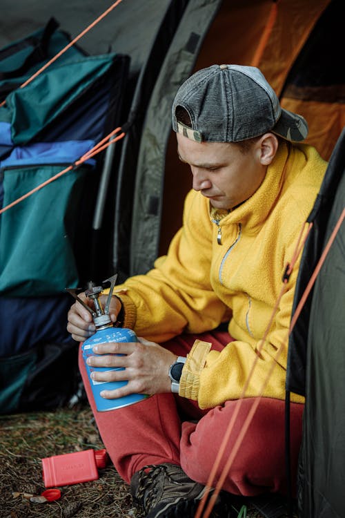 Pria Berjaket Kuning Dan Topi Rajut Hitam Memegang Smartphone Biru Dan Hitam