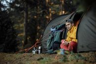 一名年轻人在露营地享受户外活动，周围是露营装备和大自然