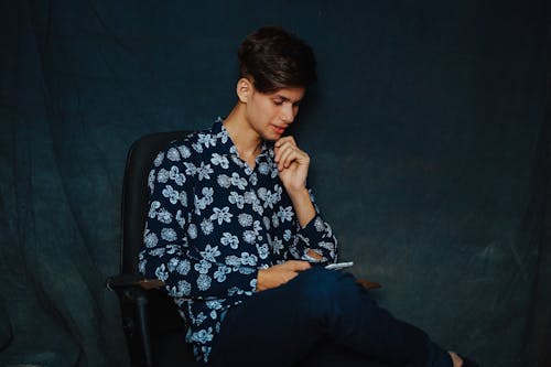 Young Man Sitting in Chair and Using Smartphone