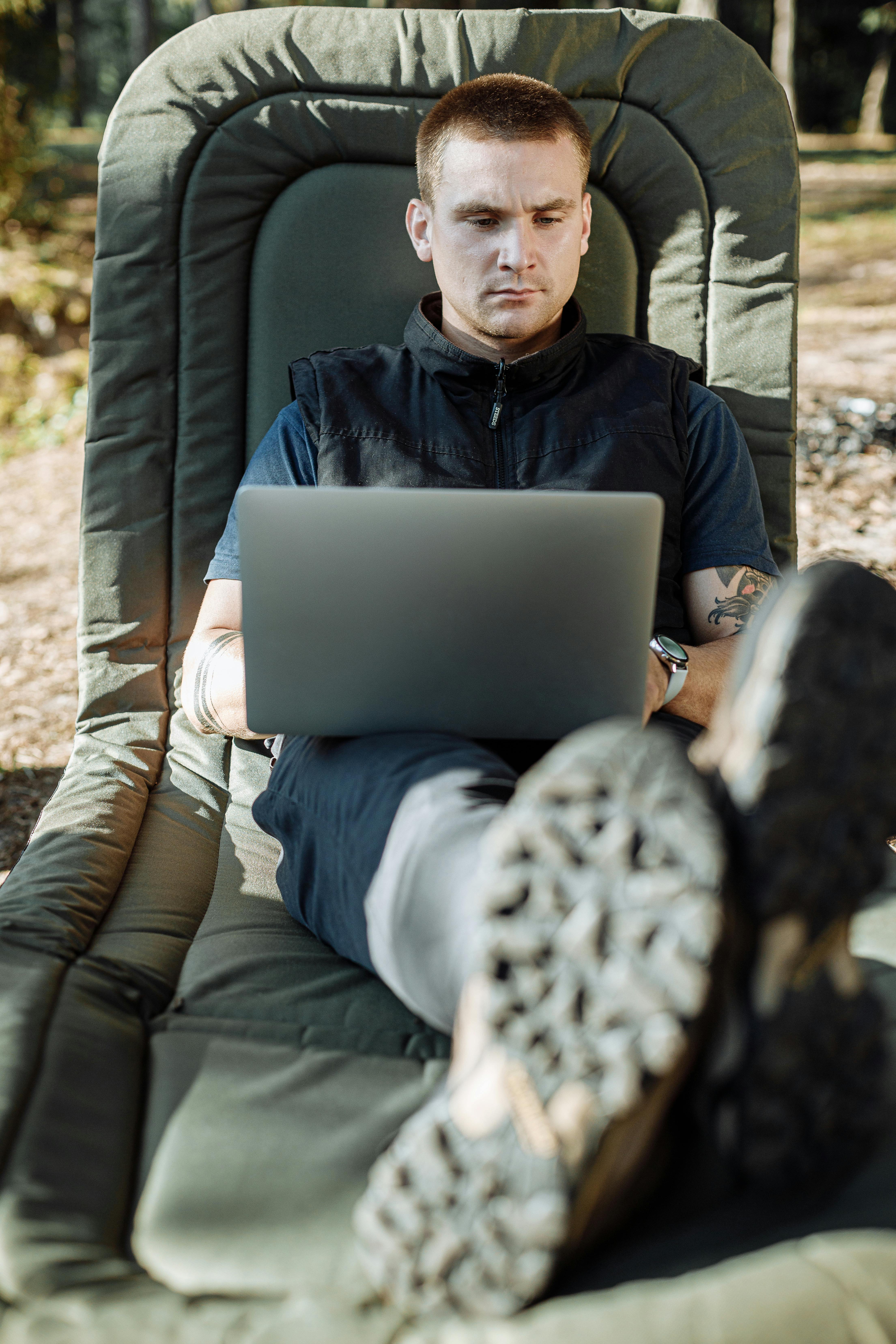 man in black jacket sitting on black leather sofa chair using macbook