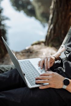 一个人在风景优美的湖畔，用笔记本电脑在户外工作，同时享受自然与科技