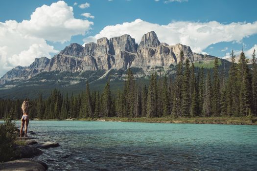Woman enjoying a peaceful view by a turquoise lake with mountains in the background.