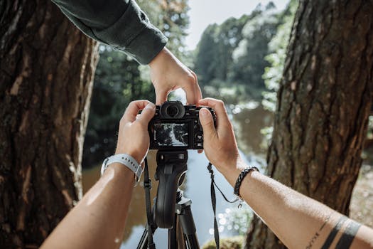 Close-up of hands setting up a camera on a tripod near a scenic forest river.