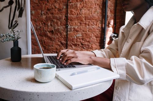 Free Woman working on a laptop with coffee in a cozy café, highlighting a productive and modern vibe. Stock Photo