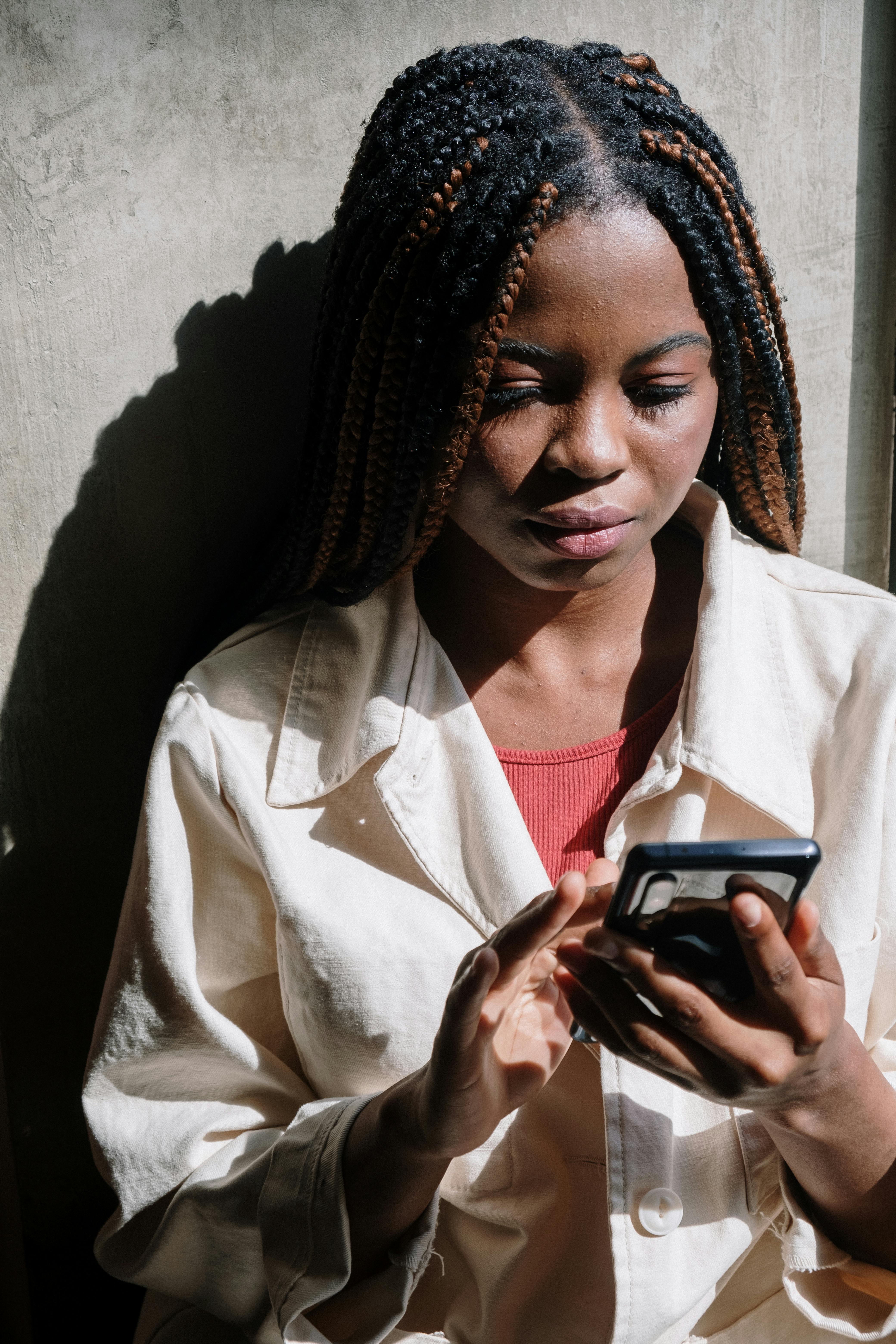 woman in white coat holding black smartphone