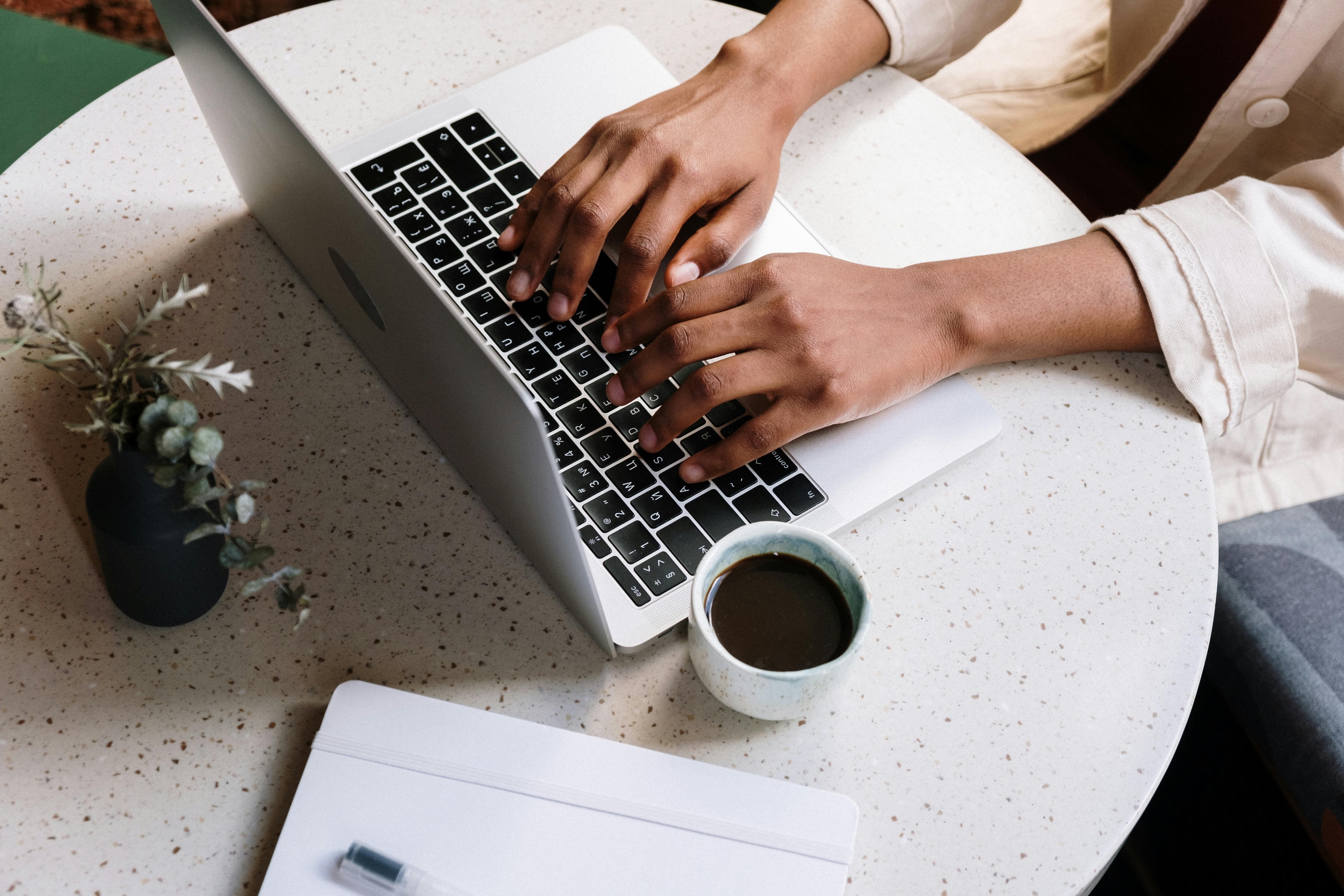 person using macbook pro beside white ceramic mug