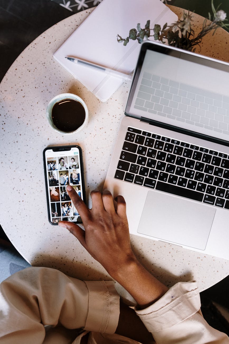 person using phone and laptop on a table with coffee cub