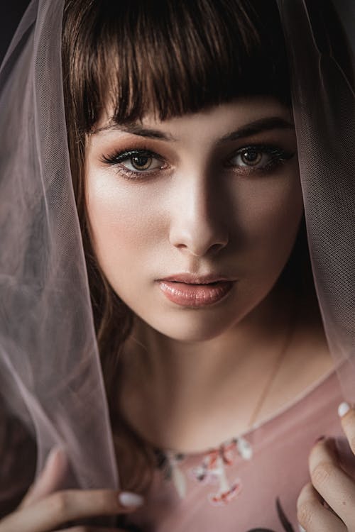 Portrait of young brown haired female with light makeup and veil on head looking at camera