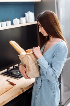 一位黑发女子在时尚的厨房里手持法棍面包，突显家居生活方式与时尚感