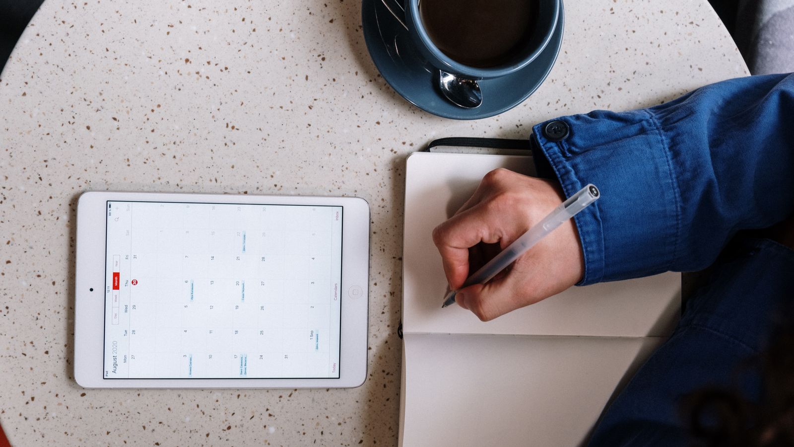 A person writing beside a tablet calendar and coffee