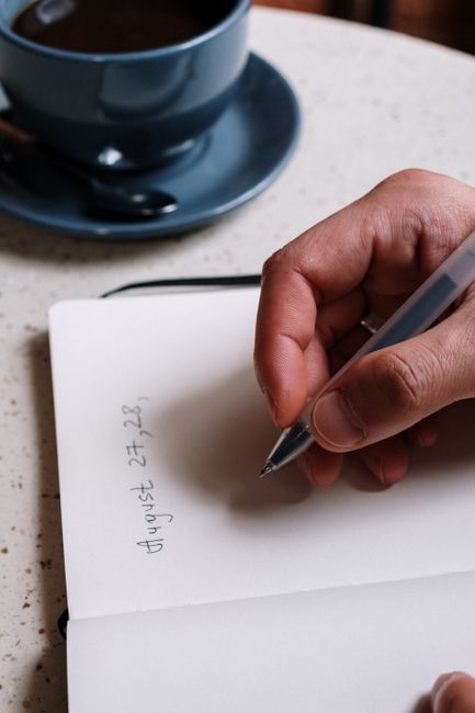 Focused view of a hand writing August dates in a planner next to a cup of coffee. - How to Create a Monthly Blog Content Calendar That Keeps You Consistent