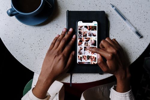 Free Close-up of hands using smartphone on a cafe table with coffee, highlighting social media browsing. Stock Photo