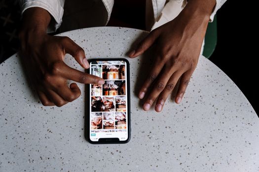 Hands interacting with smartphone displaying social media content on table in cafe setting.