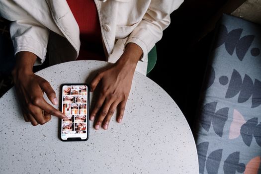 Overhead view of a person browsing photos on a smartphone at a cafe table with a touchscreen.