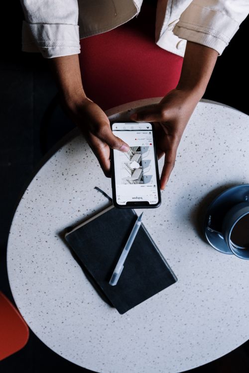 Free Person using a smartphone at a cafe table with notebook and cup. Stock Photo