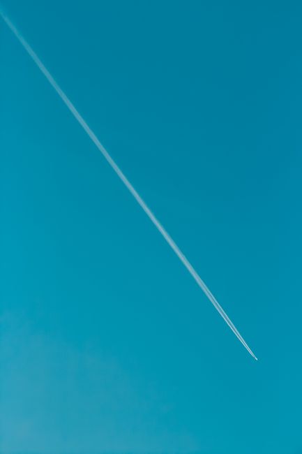 A high-flying airplane leaves a long contrail against a bright blue sky, offering ample copy space.