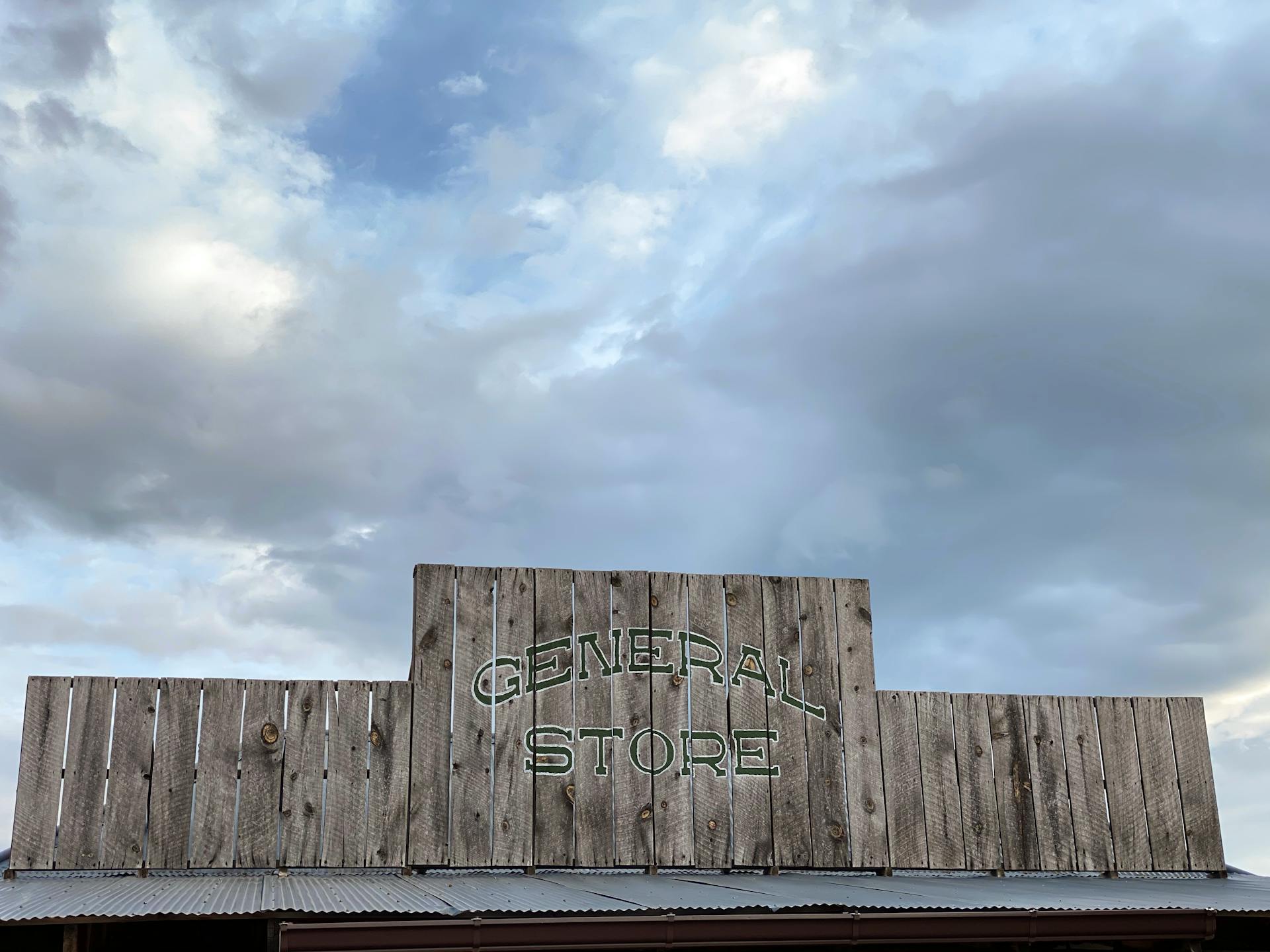 Low angle view of a rustic wooden general store sign against a cloudy sky.