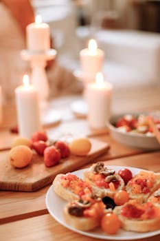 Cozy indoor setting with bruschetta, cherry tomatoes, and burning candles on a wooden table.