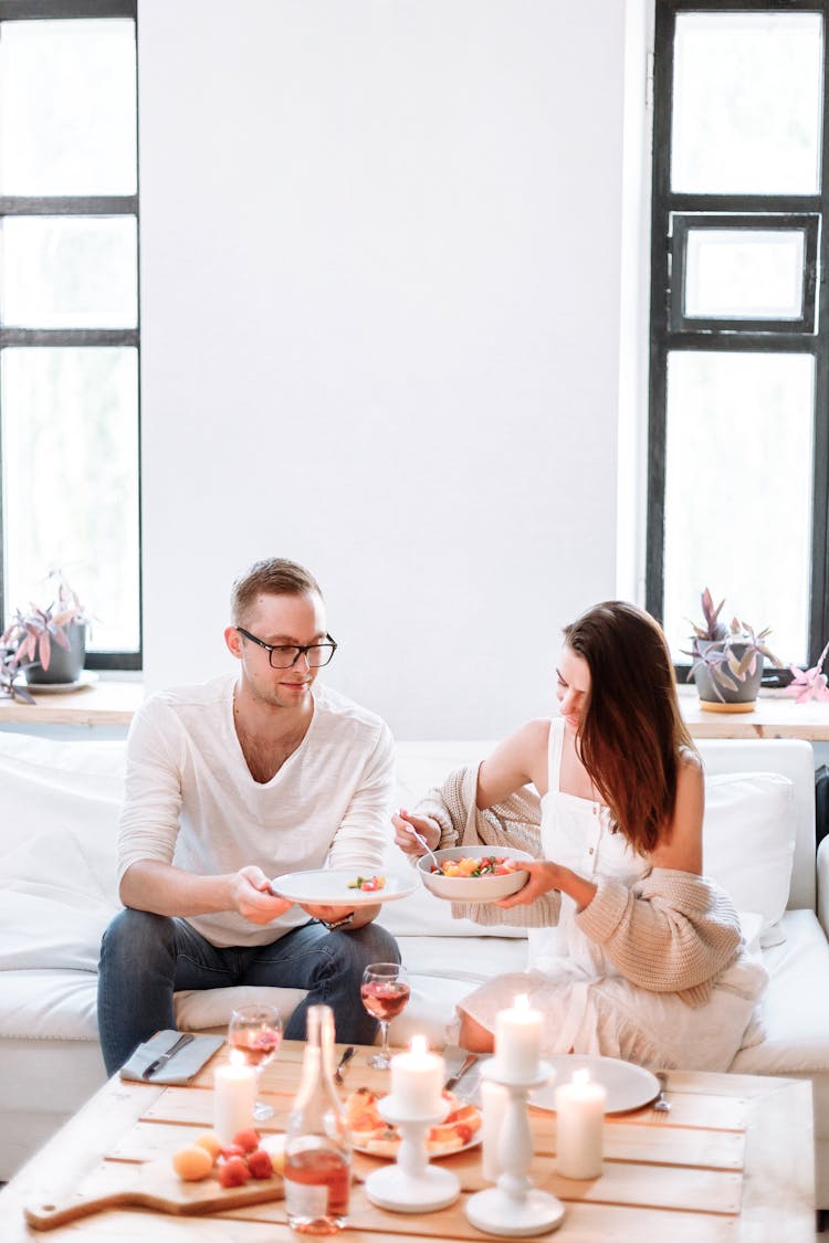 A Couple Sitting On The Couch While Holding Foods