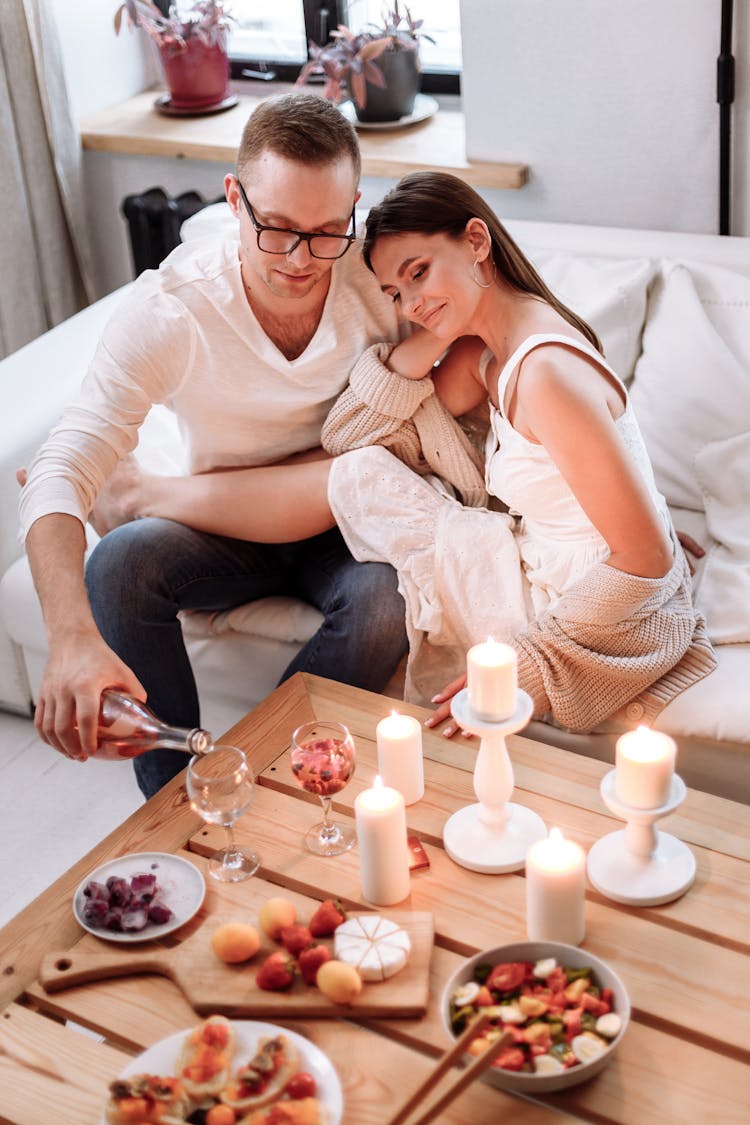 A Man Pouring Drink On A Glass While Sitting Beside Her Partner At The Couch