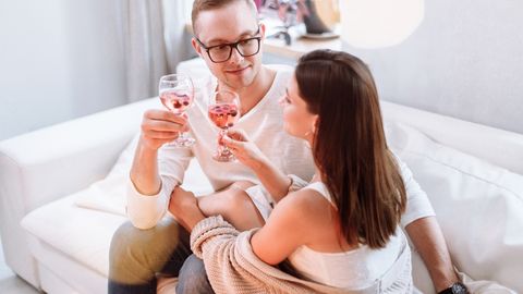 A happy couple sitting on a sofa, enjoying wine and each other's company in a cozy indoor setting.