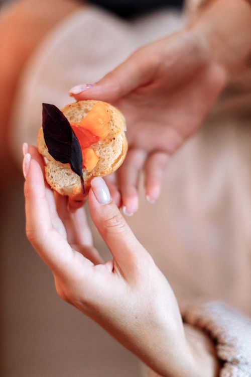 Free Close-up of a hand holding a bread slice topped with leaf and spread, showcasing culinary artistry. Stock Photo