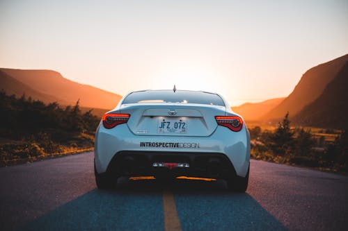 Back part of modern white automobile on paved highway road in mountains glowing with sunset light