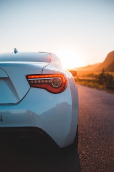 A stylish white sports car on a scenic highway at sunset, reflecting modern design and elegance.