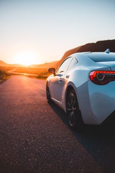 Back part of shiny white coupe car on asphalt roadway in golden sunset light