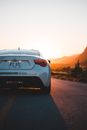 Back part of trendy white car on asphalt roadway in back lit of sundown