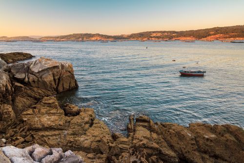 Free Tranquil scene of a lone boat in Aldán Bay, Spain, surrounded by rocky shores and calm waters. Stock Photo