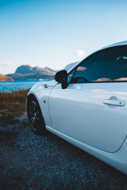 Free Side view of white vehicle parked on coast near water against blue sky with mountains in distance in daylight outside Stock Photo