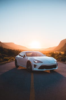 A white sports car parked on an empty mountain road during sunset offers a stunning view of freedom and travel.