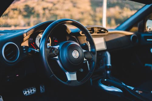 Free Black leather interior of luxury automobile with steering wheel in daylight in nature with blurred trees through windshield in daytime Stock Photo