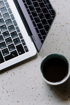 Top view of a laptop keyboard and coffee cup on a terrazzo surface.