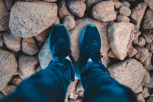 From above of anonymous tourist in sneakers wearing jeans while standing on rocks in daylight in countryside in nature outside