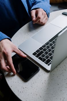 A close-up of hands exchanging phone next to a laptop on a round table.