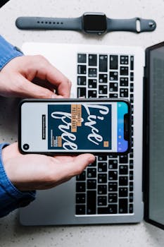 Overhead view of a smartphone displaying 'Live Free' on a laptop keyboard, beside a smartwatch.