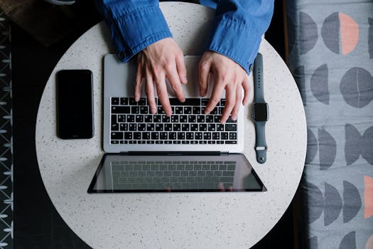 Casual setting with hands typing on a laptop, accompanied by a smartwatch and smartphone.
