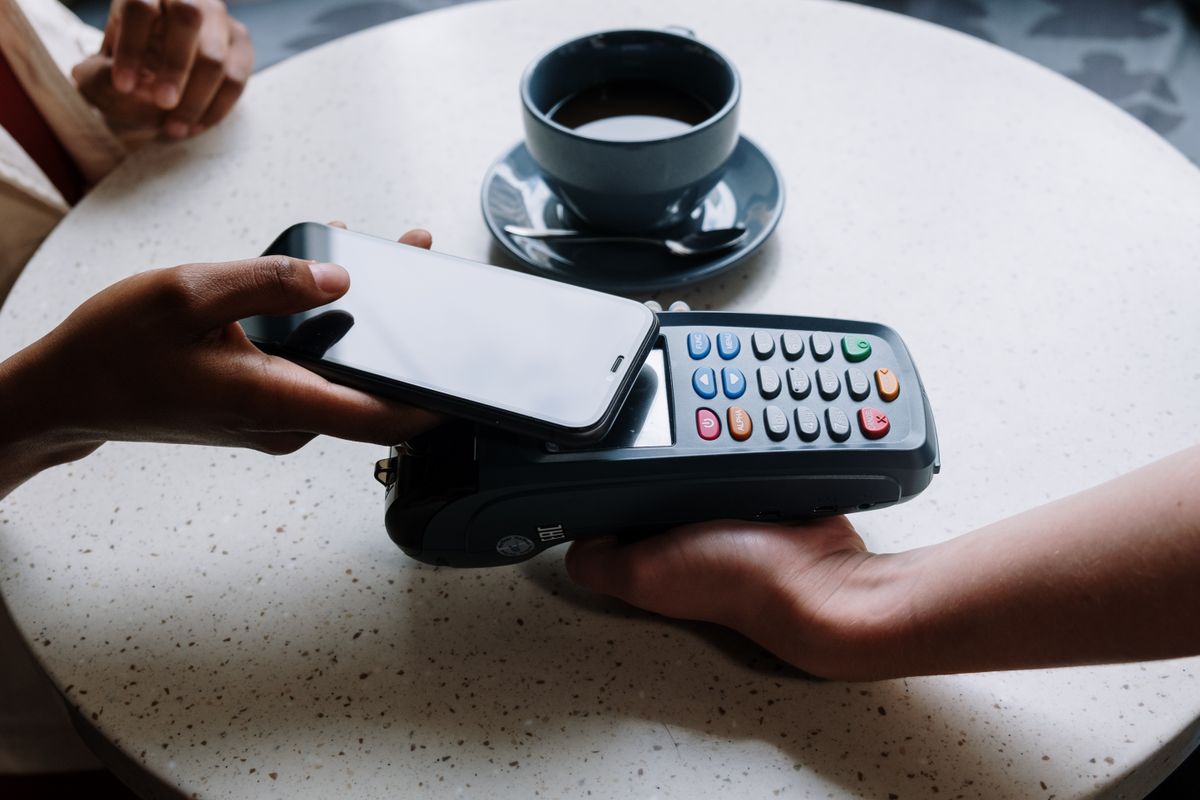 Paying with a phone at a card reader on a cafe table — photo by cottonbro studio on Pexels