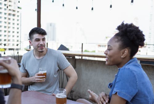 A Man in Gray Shirt Holding a Drinking Glass while Looking at the Woman Talking