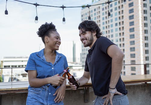 Free A Man and Woman Laughing while Holding Beer Bottles Stock Photo