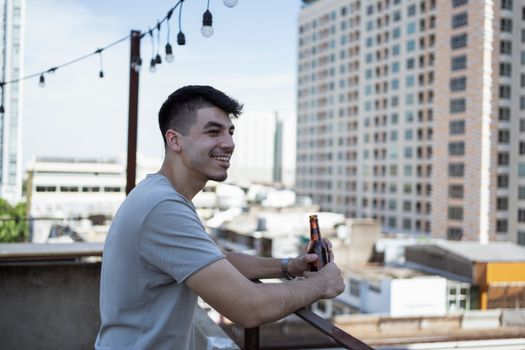 一名穿着随意的男子在城市景观屋顶露台上拿着啤酒瓶微笑