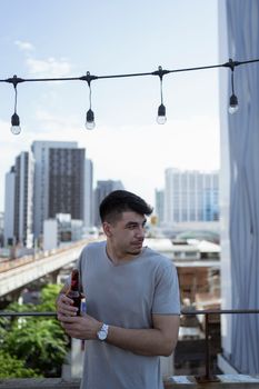 一名男子在屋顶上喝着啤酒，背景是城市天际线